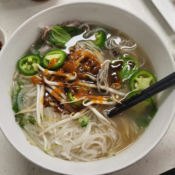 A bowl of Pho W’ Me pho with noodles, broth, meat, jalapeños, bean sprouts, and sauce.