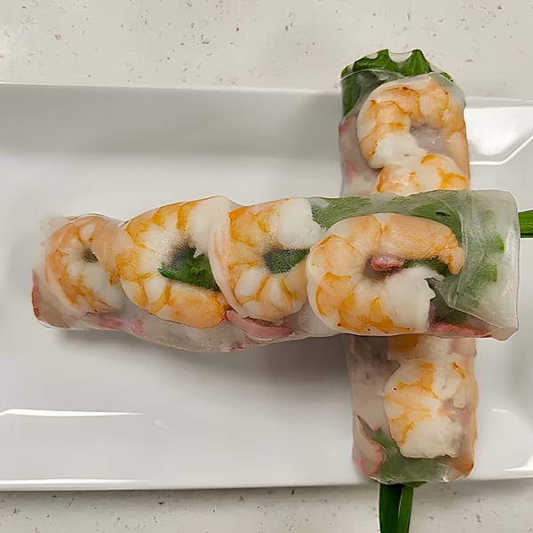 Two fresh Vietnamese spring rolls with shrimp, greens, and vermicelli, on a white plate.