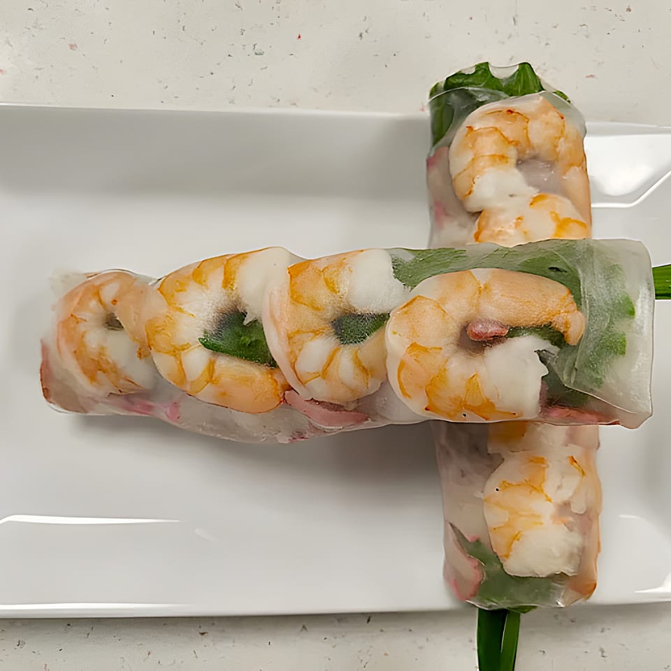 Two fresh Vietnamese spring rolls with shrimp, greens, and vermicelli, on a white plate.