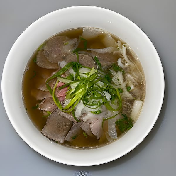 Overhead view of a white bowl filled with Pho W’ Me pho, garnished with green onions.