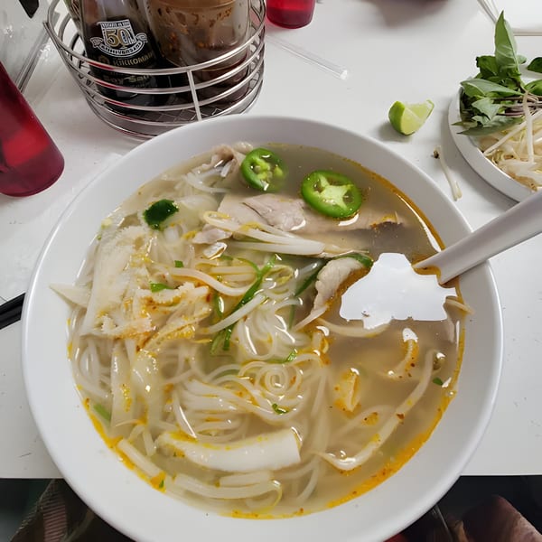 A bowl of Pho W’ Me pho with sliced jalapeños, tripe, and a side of fresh herbs.