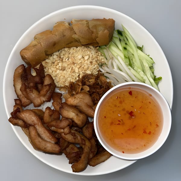 Vietnamese vermicelli bowl with grilled pork, crispy spring rolls, peanuts, vegetables, and dipping sauce.