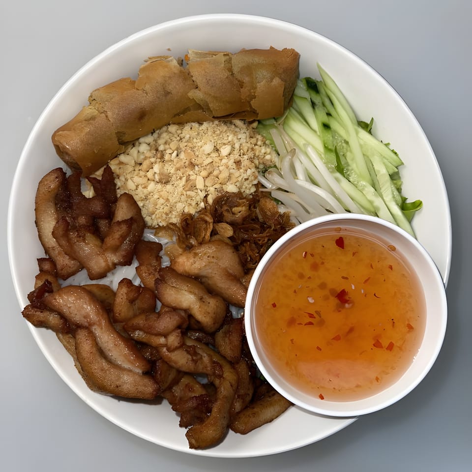 Vietnamese vermicelli bowl with grilled pork, crispy spring rolls, peanuts, vegetables, and dipping sauce.