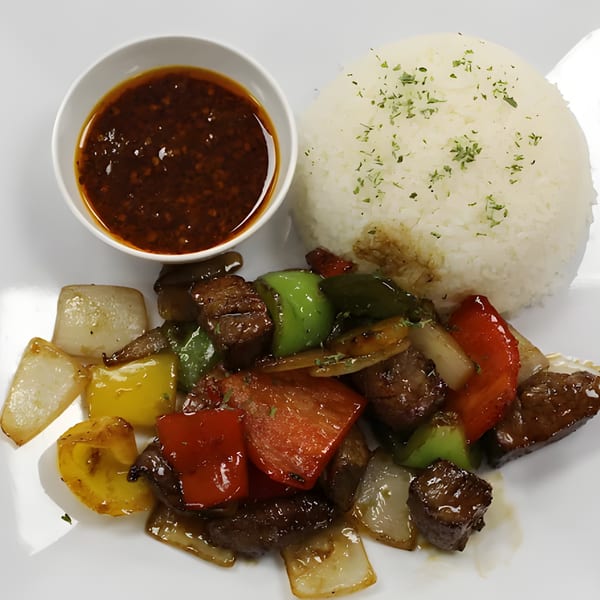Shaking beef (Bo Luc Lac) with bell peppers, onions, and rice, served with a side of sauce.