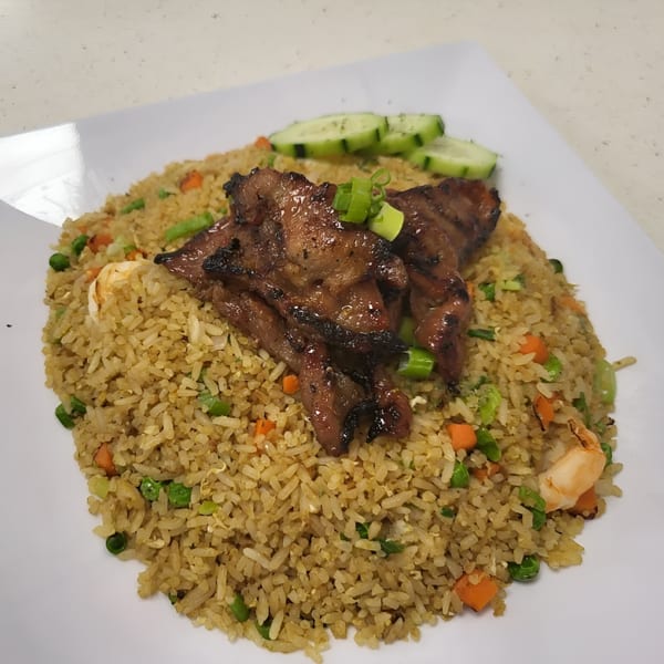 Vietnamese fried rice with grilled pork, shrimp, peas, carrots, and sliced cucumbers on a white plate.