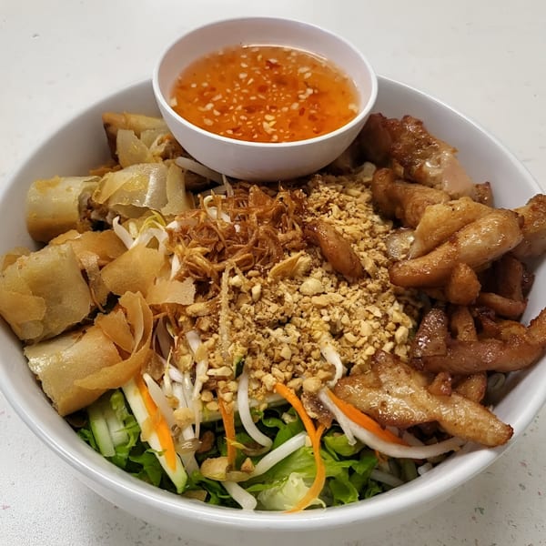 Vietnamese vermicelli bowl with grilled pork, crispy spring rolls, peanuts, and a side of sauce.